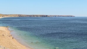 Una playa costera con aguas claras, orilla arenosa y un acantilado rocoso al fondo.