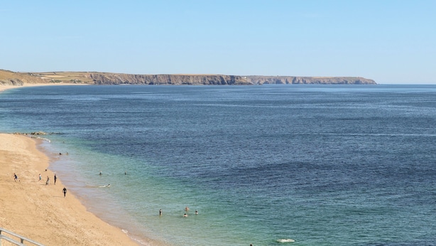 Une plage côtière aux eaux limpides, avec un rivage sablonneux et une falaise rocheuse en arrière-plan.