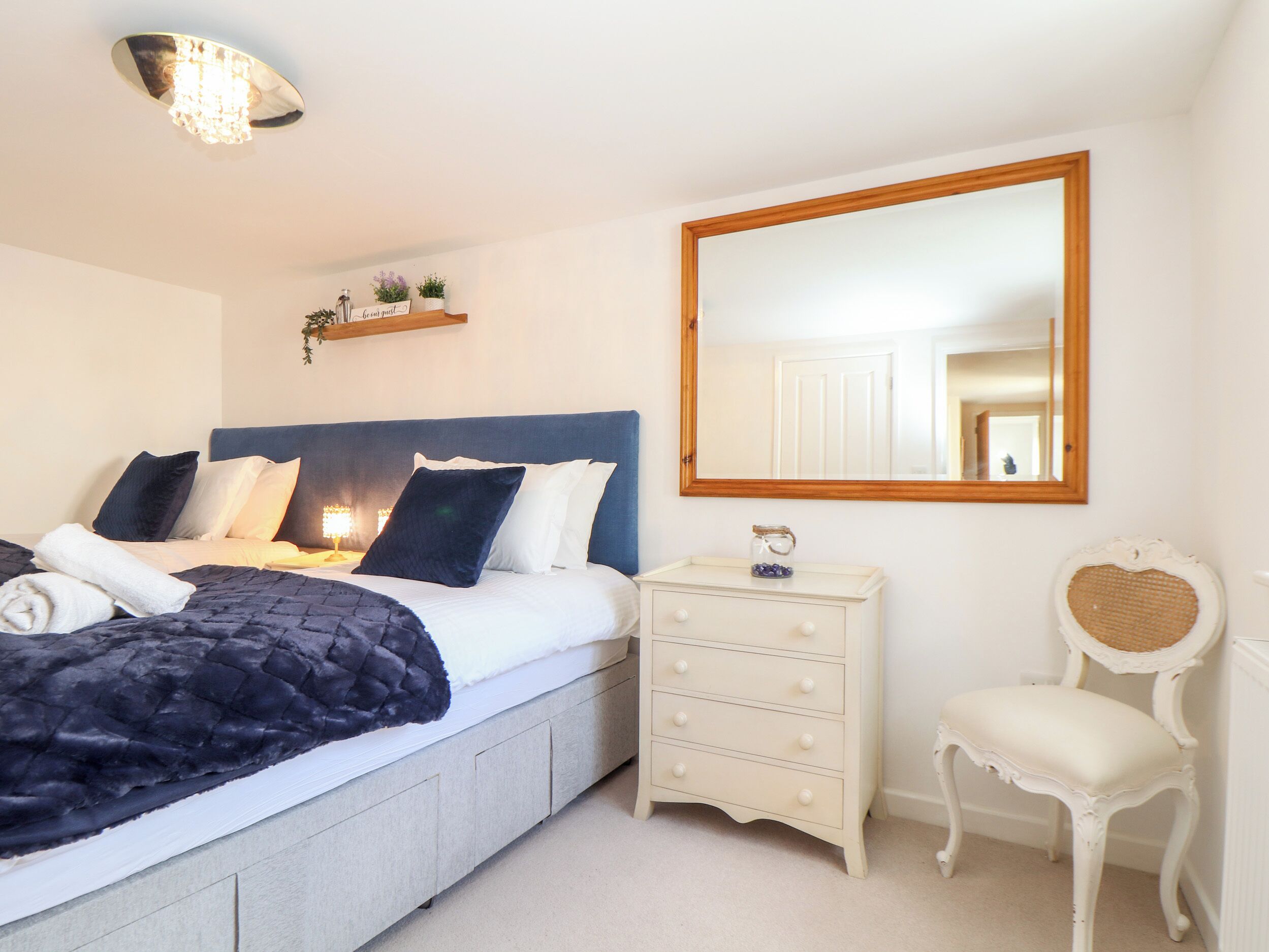 A neatly arranged bedroom with a bed, bedside table, dresser, chair, and a mirror.