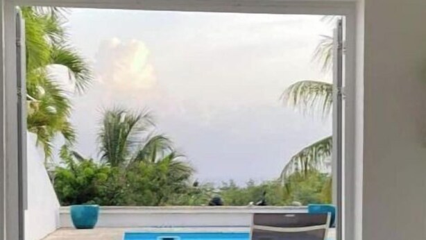 Un umbral abierto que da a una zona de piscina con una silla y una planta grande en maceta.