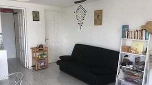 Una sala de estar con un sofá negro, una mesita de madera, una estantería y una puerta blanca.