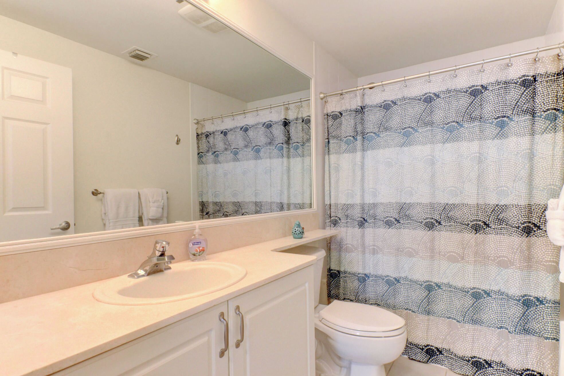 A bathroom with a white sink, mirror, and toilet. There is a patterned shower curtain and a towel rack with white towels.