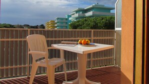 Un balcone con una sedia e un tavolo in plastica bianca, un piatto di frutta e vista su edifici a più piani sullo sfondo.