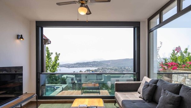 A modern living room with a large window offering a view of a city and hills. - Panoramic Villa with jacuzzi (Bodrum)