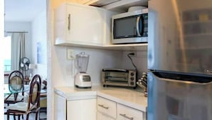 Eine kompakte Küche mit Mikrowelle, Toaster und Kühlschrank. Im Hintergrund ist ein Essbereich mit Tisch und Stühlen zu sehen.
