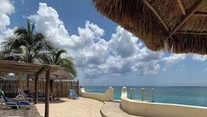 Ein Strand mit strohgedeckten Hütten, Palmen und Liegestühlen.