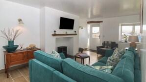 Ein Wohnzimmer mit türkisfarbenen Sofas, einem Holzschrank, einem Flachbildfernseher und einem Kamin.