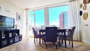 En moderne stue med fjernsyn, spiseplads og store vinduer med udsigt over byen.