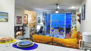 Un salon avec un canapé, une table à manger, un balcon avec vue et un ventilateur de plafond.