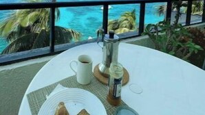 Une table avec une assiette de nourriture, une tasse et une bouteille, le tout placé devant un paysage offrant une vue sur l’océan et les palmiers.