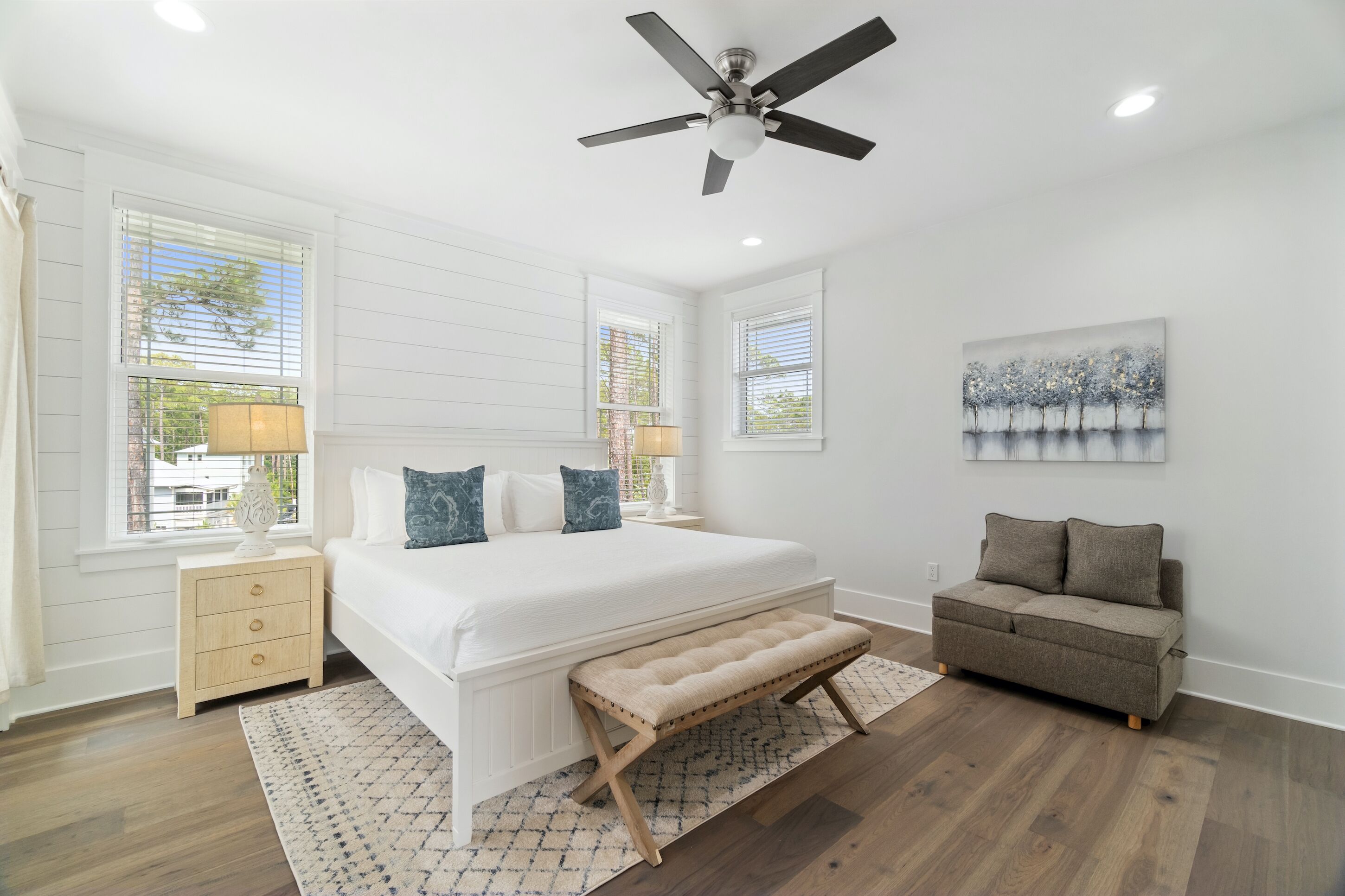 A bedroom with a large bed, a bench, a nightstand, a sofa, and a ceiling fan.
