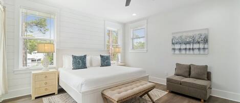 A bedroom with a large bed, a bench, a nightstand, a sofa, and a ceiling fan.