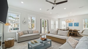 A spacious living room with a sofa, a coffee table, and a dining area with a table and chairs. - 30A Beach House - 30A Wonderland by PHG (Panama City Beach)