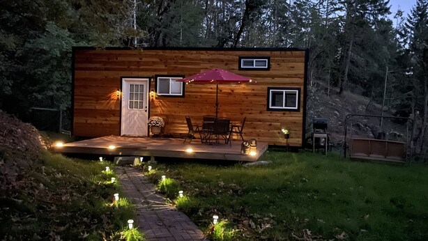 Una cabaña de madera con terraza, mobiliario exterior y un sendero iluminado con luces en el suelo.