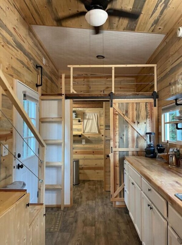 Un interior rústico de madera con una zona de cocina, armarios de madera, un ventilador de techo y una puerta corredera que da a otra habitación.