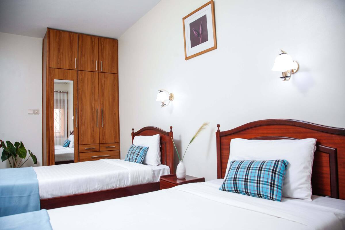 A hotel room with two beds, wooden wardrobe, bedside lamps, and a framed picture on the wall.