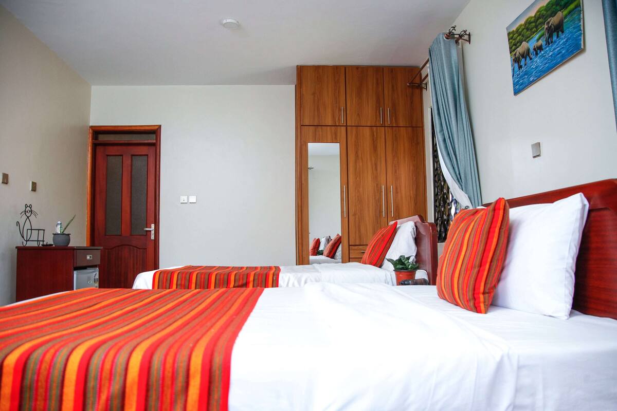 A hotel room with two beds, a wooden wardrobe, a mirror, and a painting on the wall.