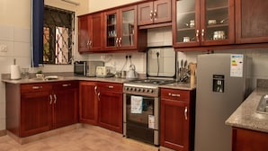 A kitchen with wooden cabinets, a stove, a refrigerator, and a microwave. - Fred and Winnie BnB (Kampala)