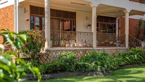 A two-story building with a covered porch, stone steps, and a variety of plants. - Fred and Winnie BnB (Kampala)