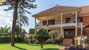 A two-story house with a balcony, surrounded by a well-maintained garden with various plants and a lawn. - Fred and Winnie BnB (Kampala)