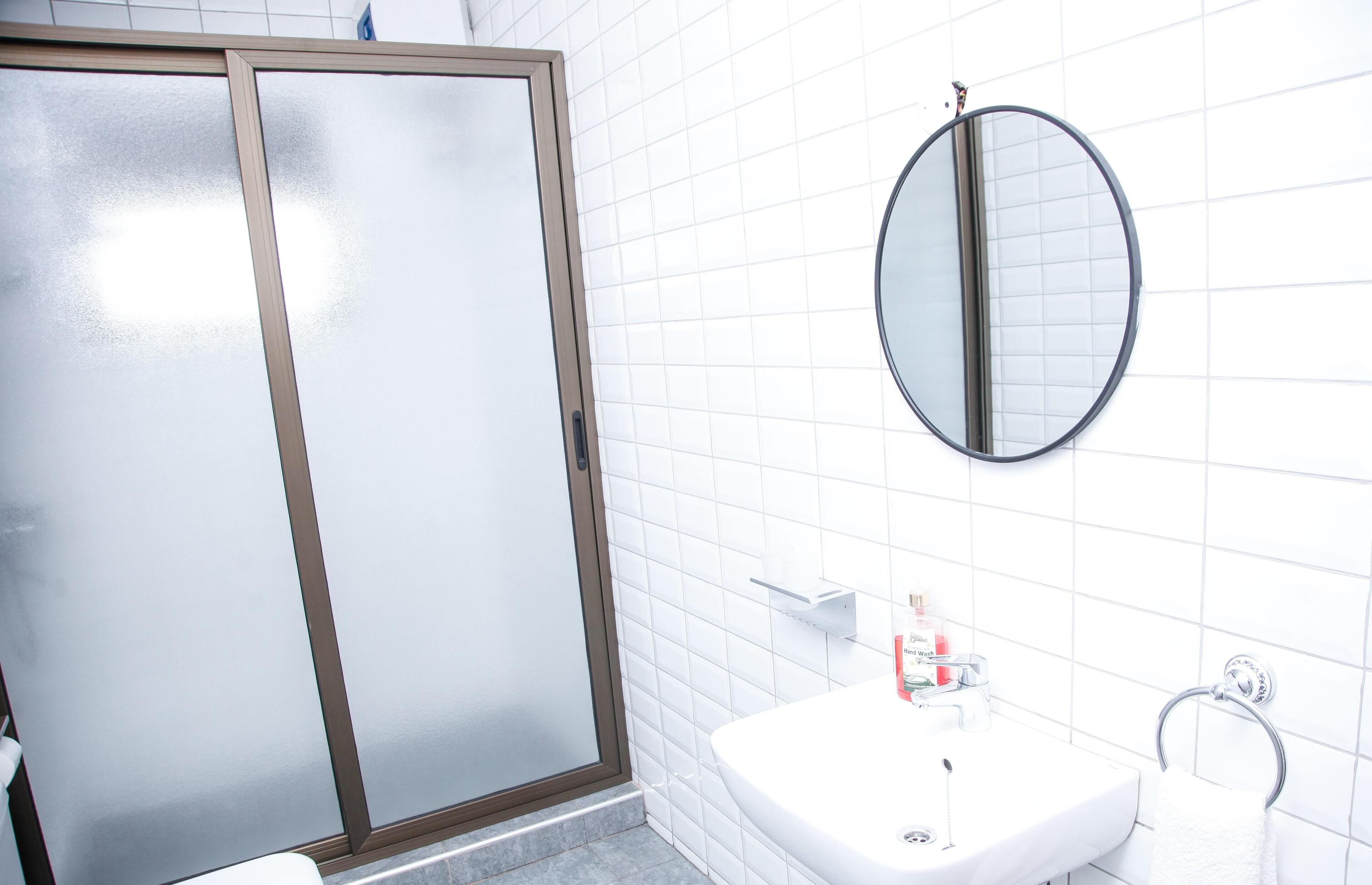 A bathroom with a glass shower door, a round mirror, and a white sink.