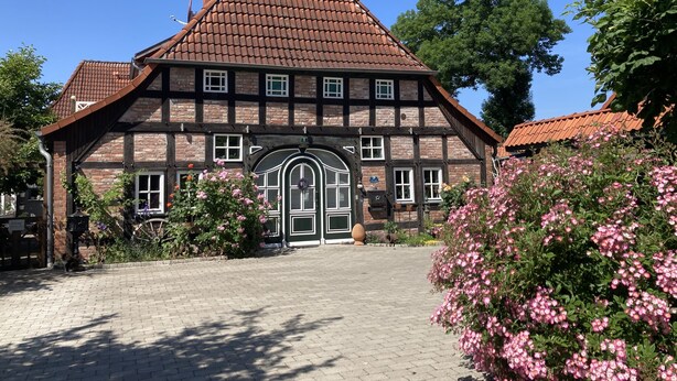 A traditional half-timbered house with a steeply pitched roof, a central entrance with a decorative arch, and a brick pathway leading to the door. - Cozy vacation apartment with complete equipment for up to 5 people (Bötersen)