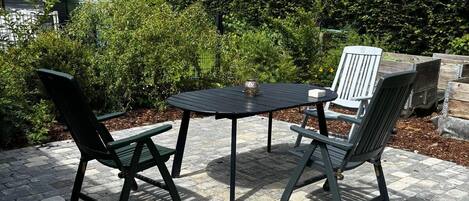 A patio with a round table and four chairs, surrounded by a brick border and greenery.