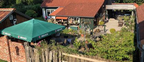 A rustic building with a red-tiled roof, a wooden fence, and a green umbrella labeled "BECK'S".