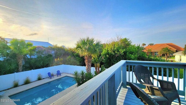 Un patio trasero con piscina, sillas de cubierta azules y barandilla de madera.