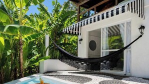Una hamaca en un área junto a la piscina, con vista a una casa y abundante vegetación.