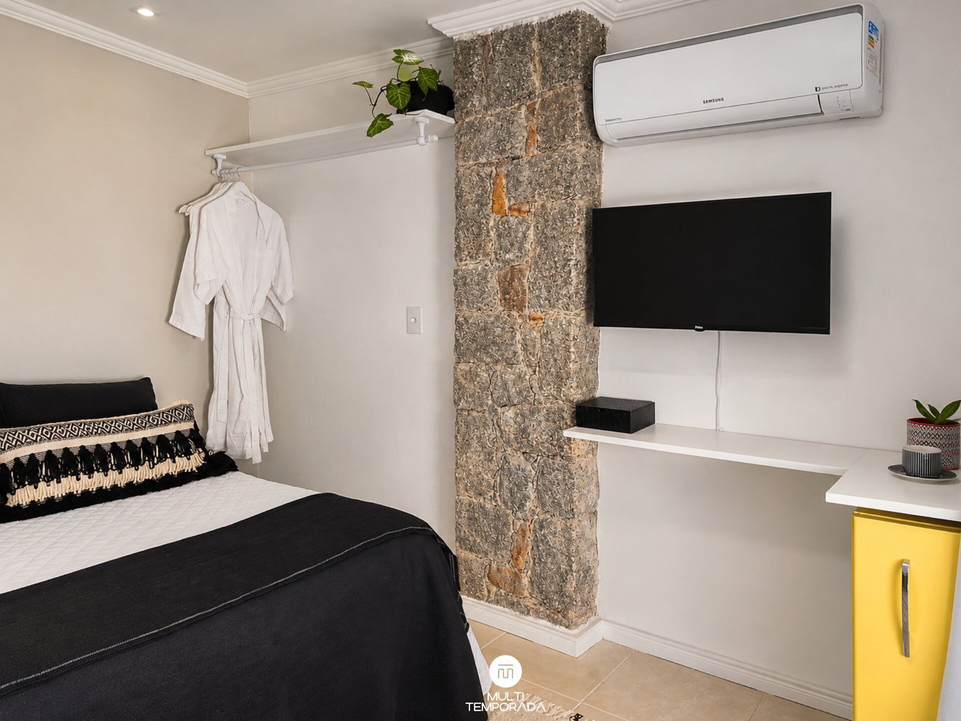 A bedroom with a bed, a TV, an air conditioner, a plant, and a yellow cabinet.
