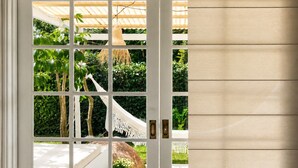 Puerta blanca con diseño de cuadrícula, que da a un espacio exterior con una hamaca, follaje y una pérgola de madera.
