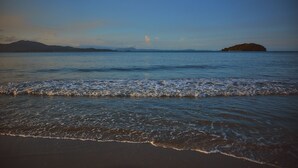 Una playa con olas suaves, una isla distante y montañas al fondo.
