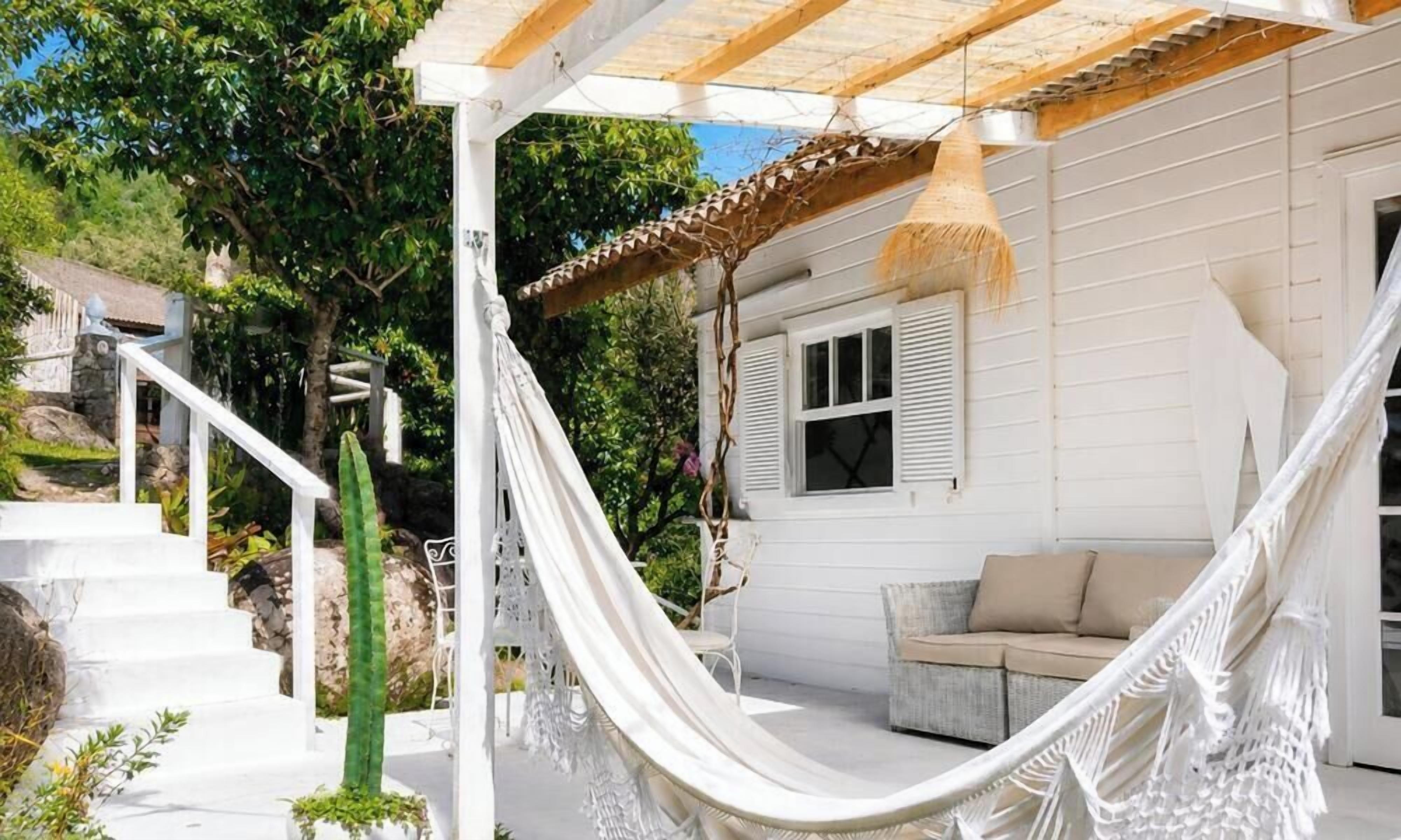 A white house with a porch, a hammock, and a staircase leading to a door.