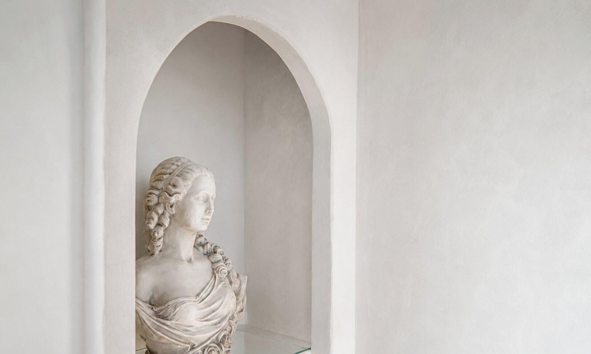 A marble bust sculpture in a niche with a simple, clean background.