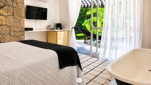 Un dormitorio con cama, televisión, minibar y vistas a zonas verdes a través de una puerta corrediza.