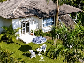 A house with a tiled roof, a front porch, and a small garden with a lawn and palm trees. - CasaIvan (Florianópolis)