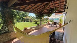 A hammock hanging under a wooden pergola with a patio area, outdoor furniture, and a view of a garden. - Relax in Casa Pousadela with Garden 5 km from the sea (Nogueira Da Regedoura)