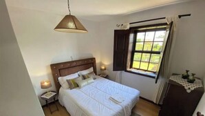 A bedroom with a large bed, a bedside lamp, a nightstand, a window with curtains, and a wooden headboard. - Relax in Casa Pousadela with Garden 5 km from the sea (Nogueira Da Regedoura)