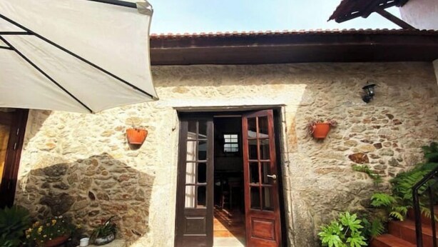 A stone building with a wooden door, potted plants, and a blue chair outside. - Relax in Casa Pousadela with Garden 5 km from the sea (Nogueira Da Regedoura)
