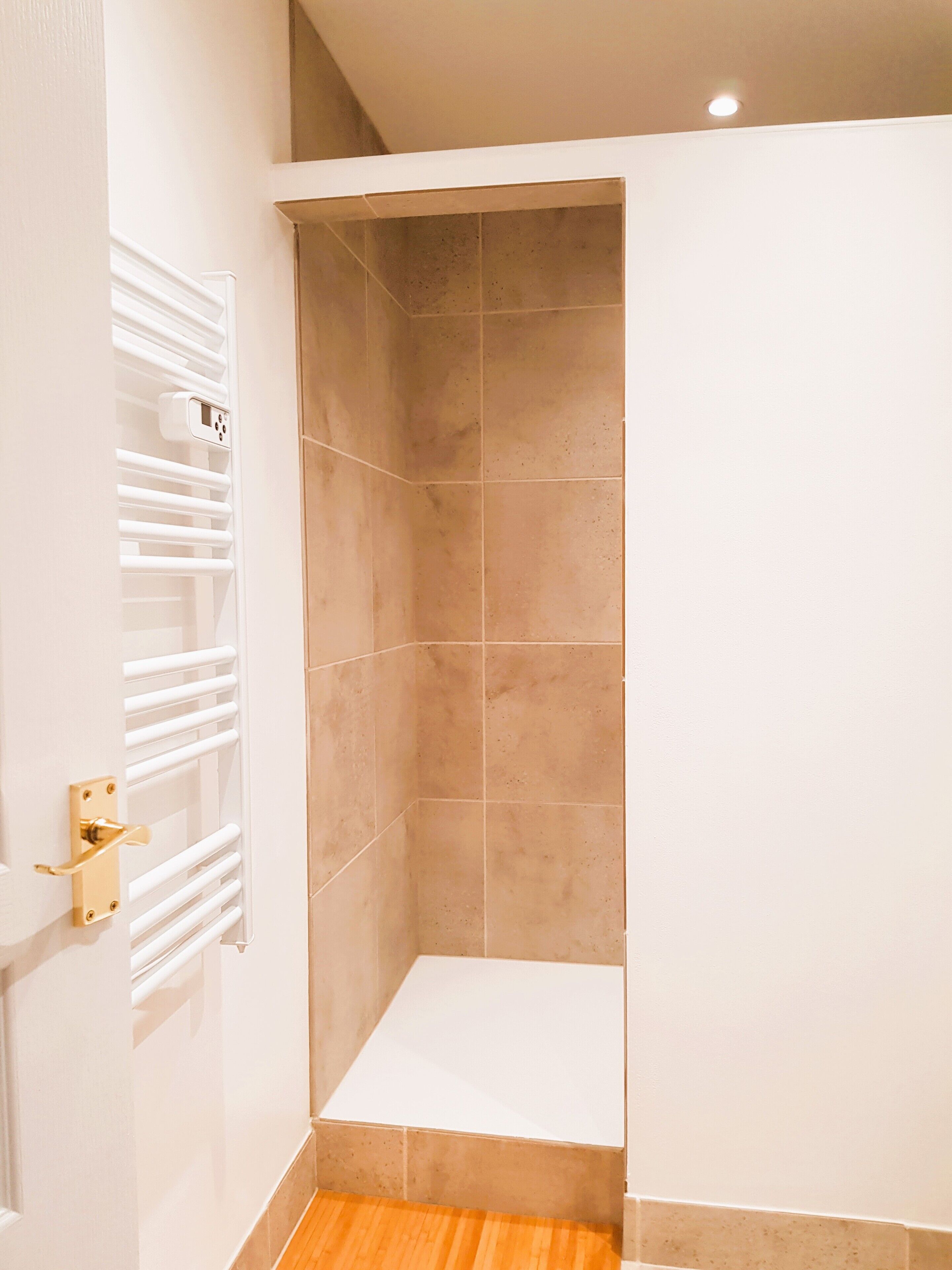 A bathroom with beige tiles, a white radiator, and a wooden floor.