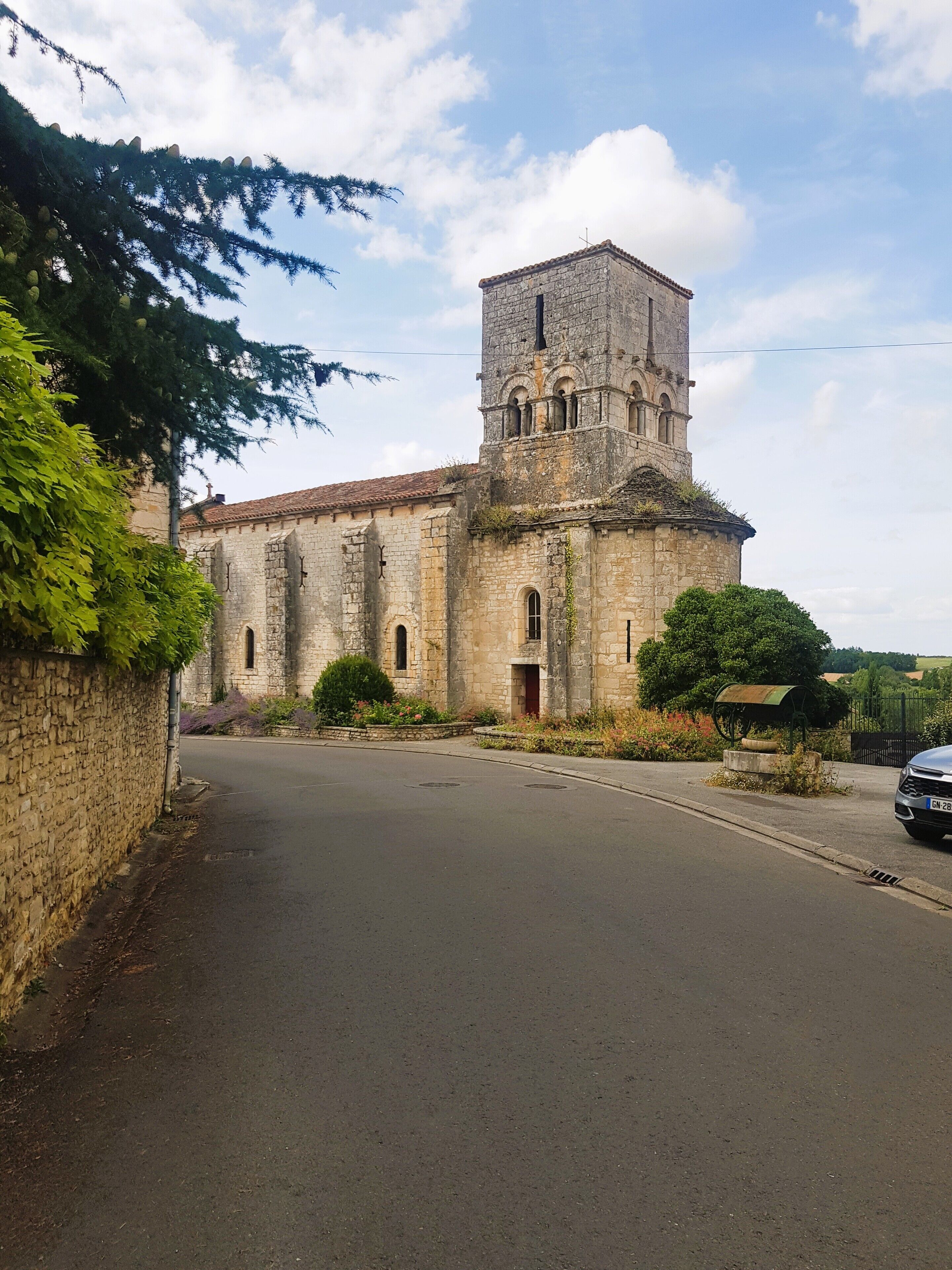 A historic stone building with a central tower, a paved road in front, and a car parked nearby.