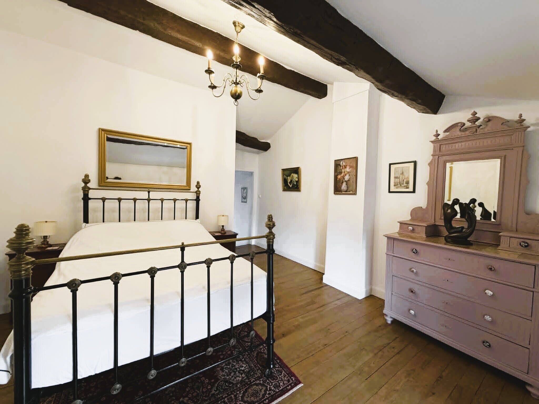 Un dormitori amb un llit, una petita taula de nit, una pèndol i quadres a les parets.