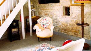 A living room with a stone wall, a white staircase, a flat-screen TV, a floral armchair, a patterned rug, and a small table with a lamp. - Charming Cottage with exclusive use of the Jacuzzi upon request
 (Val-de-Bonnieure)