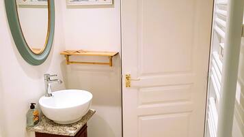 Een badkamer met een wit wastafelmeubel, een spiegel met een groene lijst, een deur en een klein plankje boven de wastafel.