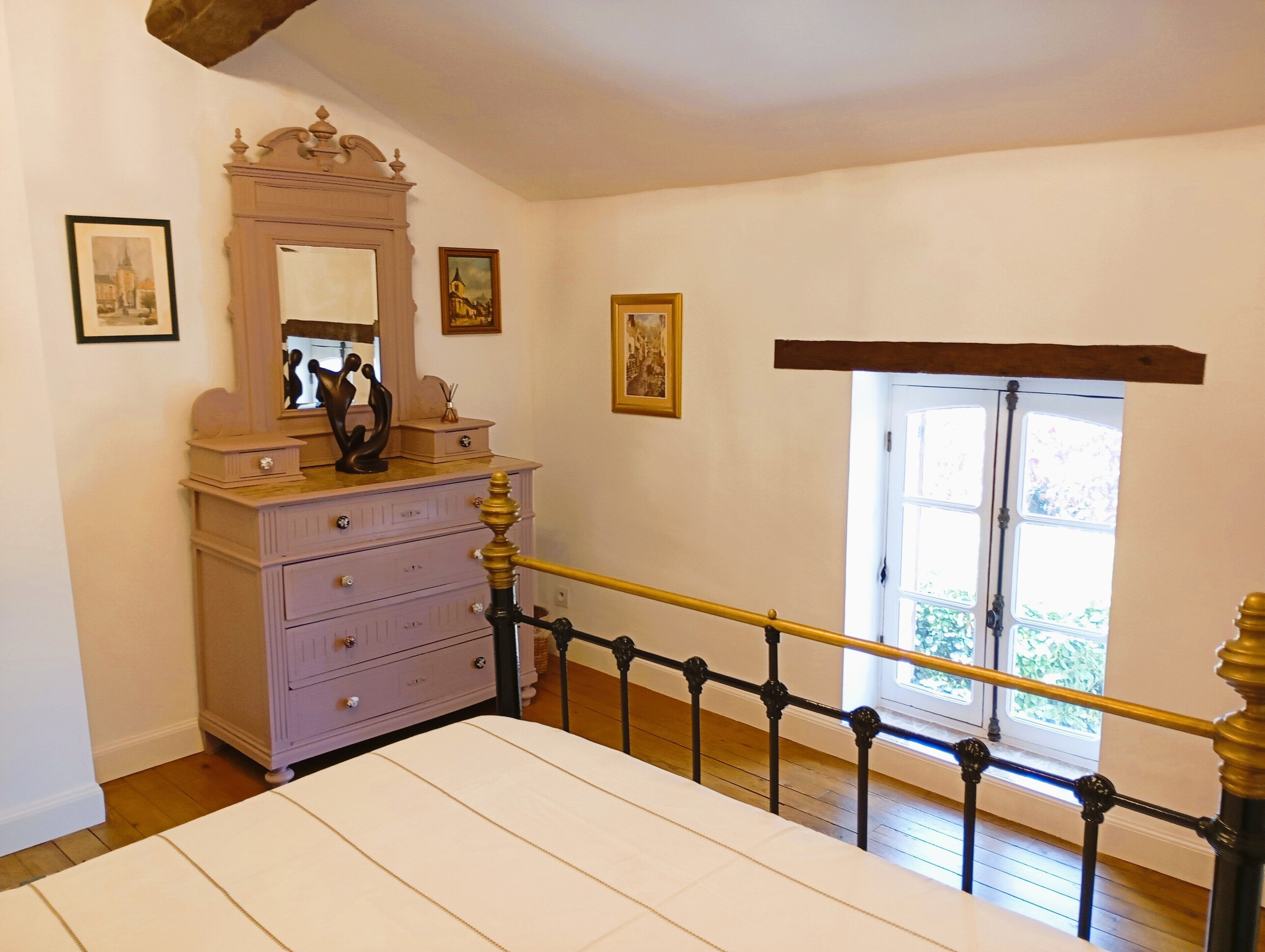 Un dormitorio con cama, tocador, espejo y ventana con vista a la vegetación.