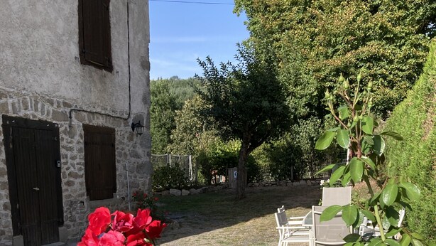 Ein Steinhaus mit einem Garten, der rote Rosen und eine Sitzgelegenheit mit Stühlen zeigt.