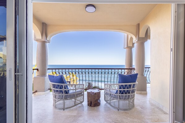 Enjoy the ocean view from this balcony with two comfortable chairs and a stool.