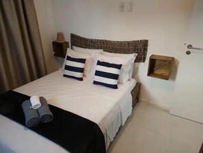 A neatly made bed with striped pillows, a black and white bedspread, and rolled towels on the side. - Paradise is waiting for you (Sap Miguel dos Milagros)