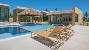 Ett modernt semesterkomplex med en swimmingpool, solstolar och parasoller med halmtak.